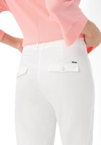 Witte broek met een getailleerd ontwerp, voorzien van twee achterzakken met knoopsluitingen en een merklabel. Textuurstof met een gladde afwerking.