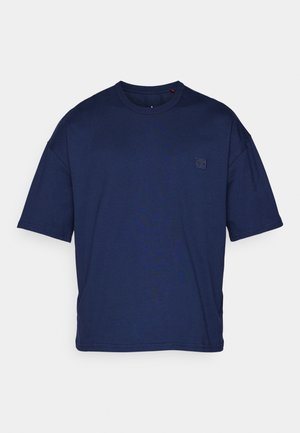 Camiseta de algodón azul marino de manga corta con cuello redondo y pequeño parche de logo cosido en el lado izquierdo del pecho.