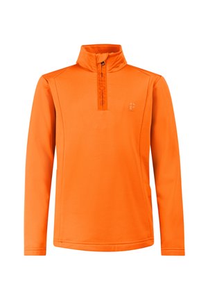Jongen staat met handen in de zakken, draagt een oranje trui, zwarte en grijze broek, zwarte laarzen en een zwarte muts tegen een effen achtergrond.