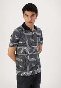 Polo de rayas blancas y negras con patrones geométricos, mangas cortas, un cuello negro y un diseño ajustado.
