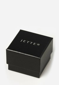 Scatola per gioielli nera con finitura testurizzata, caratterizzata dal logo argentato "JETTE" sulla parte superiore. Bordo sicuro e liscio, design compatto.
