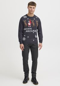 Dunkelgrauer gestrickter Pullover mit festlichen Rentieren, Schneeflocken und dem Text "ROCK'N AROUND". Kombiniert mit schwarzen engen Hosen und Lederstiefeln.