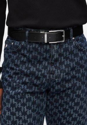 Jeans en denim bleu avec un motif pied-de-poule en bleu clair, accompagnés d'une ceinture en cuir noir avec une boucle en métal argenté.