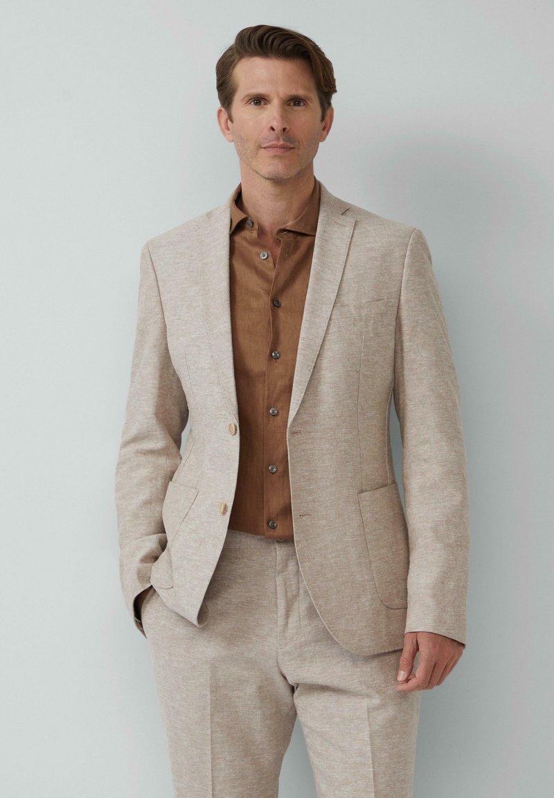 Beige colbert met textuurstof, enkele knoopsluiting en notch-lapels, gecombineerd met een bruine overhemd en bijpassende broek.