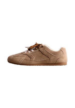 Vue de profil d’une chaussure basse en daim beige, avec des lacets marron, des empiècements cousus, un col rembourré blanc et une semelle en gomme, sur fond blanc.