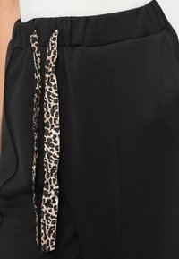 Zwarte joggingbroek met een elastische tailleband, voorzien van een drawstring in luipaardprint en zijzakken. Zachte textuur en een ontspannen pasvorm.