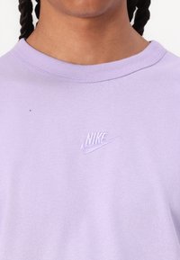 Lila pamut póló, kerek nyakkal, rövid ujjal, és egy kis hímzett Nike logóval a mellrészen. Puha tapintású, sima felületű.