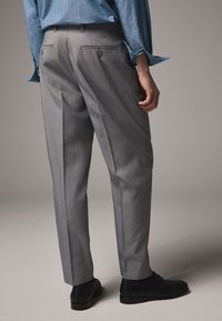 Pantaloni grigi chiaro su misura con una texture liscia, davanti piatto e due tasche posteriori, abbinati a scarpe eleganti nere.