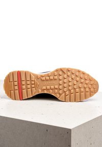 Shoe sole in tan rubber with varied tread pattern, red stripe near heel, and "LLOYD" logo embossed in center.