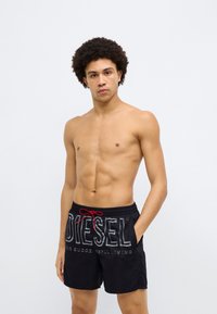 Mustad ujumispüksid punase nööriga, ees suur valge "DIESEL" logo ja tekst, valmistatud kergest kangast.