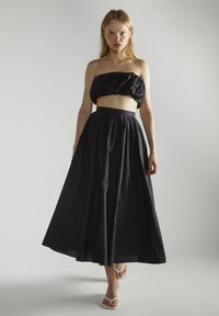 Conjunto negro de dos piezas que incluye un top corto sin mangas con volantes y una falda larga de talle alto y fluida, hecha de una tela ligera.
