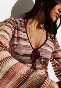 Top de manga larga con un escote en V profundo, que presenta patrones tejidos multicolores intrincados en tonos de rosa, granate y verde, con un detalle de lazo.