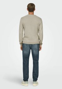 Beige gestructureerde trui met een ronde halslijn, gedragen met donkerblauwe jeans. De trui heeft ribgebreide manchetten en een zoom, wat de casual uitstraling aanvult.