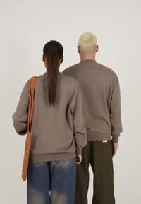 Sweatshirt din bumbac maro cu manșete și tiv ondulate, asociat cu blugi albaștri. Accesoriu: geantă texturată portocalie.