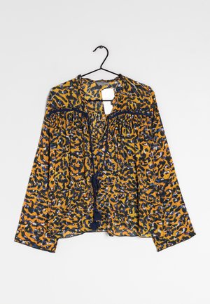 Lange mouwen blouse met geel, blauw en zwart abstract patroon, voorste strikkoordjes met kwastjes en losse pasvorm, hangend aan een zwarte hanger.