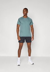 Light blue athletic t-shirt with short sleeves, round neck, and subtle logo. Paired with black shorts and white sneakers. Smooth texture.