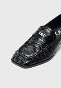 Mustast nahast loafer, millel on reljeefne tekstuur, ruudukujuline nina ja hõbedane aksentdetail paelal. Kummist tallaosaga, kergelt soonitud.