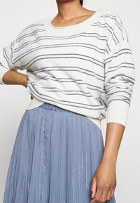 Vit tröja med marinblå ränder, rund halsringning och ribbad ärm, ihop med en plisserad, golvlång blå kjol med glans.