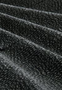 Gros plan d'un tissu gris foncé avec une texture douce et duveteuse et un motif moucheté plus clair subtil dans des plis diagonaux.