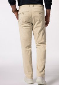 Beige bomullsbukser med rak passform, som har två bakfickor och en slät, texturerad yta. Bärs med vita sneakers.