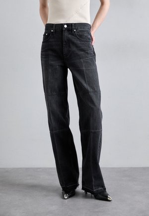Black denim wide-leg jeans with a high waist, contrasting seams, and raw hem. Paired with pointed-toe black shoes.