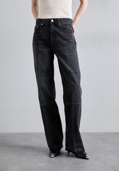 Black denim wide-leg jeans with a high waist, contrasting seams, and raw hem. Paired with pointed-toe black shoes.