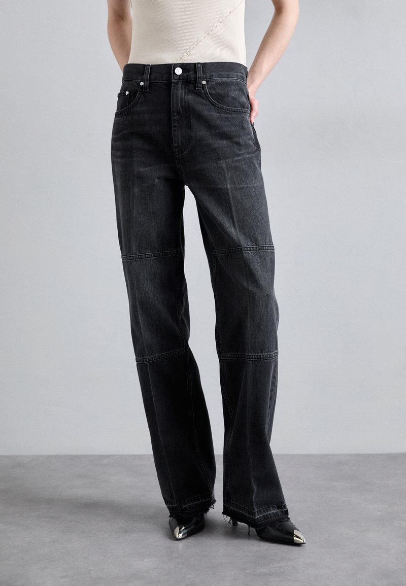 Jean large en denim noir à taille haute, with des coutures contrastantes et un ourlet brut. Associés à des chaussures noires à bout pointu.