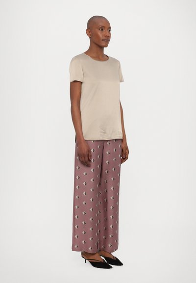 Top bege de manga curta combinado com calças largas rosas estampadas com formas geométricas em diamante. Sapatos de salto pretos slim completam o look.