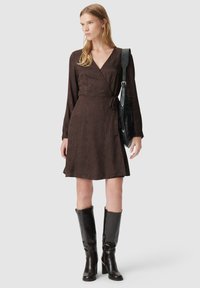 Braunes Wickelkleid mit einem dezenten Muster, langen Ärmeln und einem Gürtel in der Taille. Kombiniert mit knielangen schwarzen Lederstiefeln.