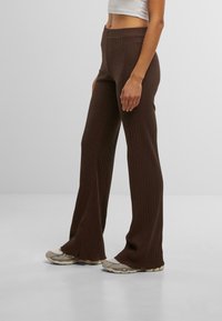 Pantalons évasés côtelés marron à taille haute, en tissu texturé et silhouette ajustée, assortis à des baskets claires.
