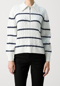 Weißer Kabelstrickpullover mit marineblauen horizontalen Streifen, halblangem Reißverschlusskragen, geripptem Saum und Ärmel. Der Stoff scheint weich und strukturiert zu sein.