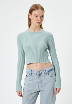 Pull court en ribbed bleu clair avec des manches longues, texture douce, encolure ronde, associé à un jean en denim délavé taille haute avec des motifs en losange.
