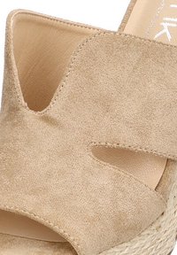 Sandalia de cuña de ante beige con punta abierta y diseño recortado. Presenta una plantilla texturizada y una suela intermedia de fibra trenzada para un detalle añadido.