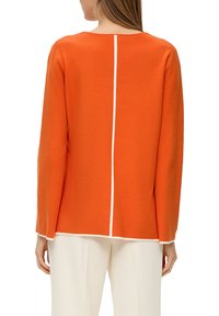 Oranje trui met een ronde hals, lange mouwen en een witte middennaad. Zachte textuur en rechte snit. Draag het met witte geribde broek.