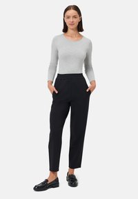 Długi jasnoszary top z długim rękawem oraz czarne spodnie z elastycznym pasem, wyposażone w boczne kieszenie i zwężane nogawki. Czarne mokasyny.