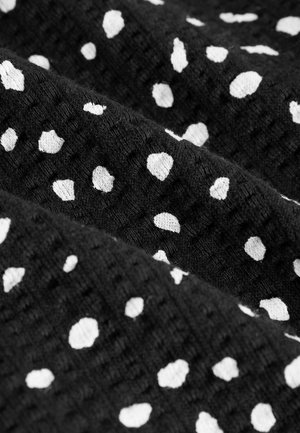 Zwarte stof met een gestructureerde weving, gekenmerkt door verspreide witte vlekken in verschillende maten. Het patroon zorgt voor een contrast op het oppervlak.