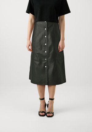 Black cropped top paired with a knee-length, dark green leather skirt featuring silver buttons down the front. Black strappy heeled sandals.