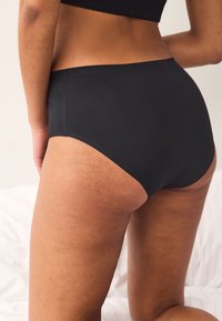 Czarne figi z wysokim stanem o prążkowanej fakturze, z gładkimi krawędziami i dopasowanym krojem. Tkanina wydaje się miękka i elastyczna.