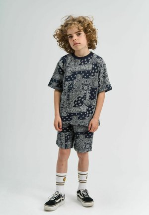 Námorníckom modrý vzorovaný outfit pozostávajúci z trička s krátkym rukávom a šortiek, s zložitými bielymi dizajnami. Nosený s čiernymi teniskami a bielymi ponožkami.