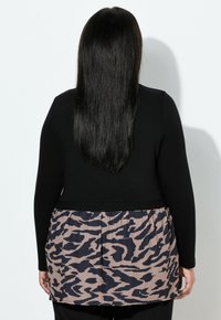 Top negro de manga larga con peplum estampado de leopardo en beige y azul oscuro. Textura suave; cuerpo entallado con una sección inferior acampanada.