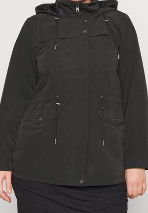 Sort hættejakke med frontlynlås og trykknapper, justerbare snore i taljen, klaplommer, båret af person med synlige hænder.