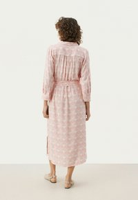 Robe longue rose avec motif floral, tissu léger, léger éclat, manches longues, taille cintrée et fentes sur les côtés pour faciliter le mouvement.