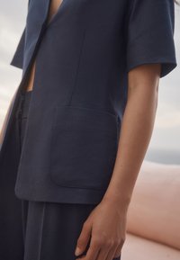 Haut bleu marine à manches courtes avec col en V, doté d'une grande poche plaquée et d'une coupe décontractée, fabriqué en tissu texturé.