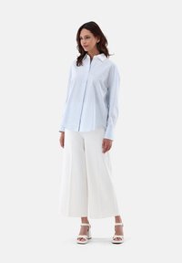 Light blue striped button-up shirt with a white collar, paired with white wide-leg pants and strappy white heeled sandals.