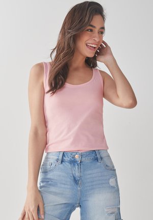 Ljusrosa ärmlös tanktop, tillverkad av mjukt material, med rundad halsringning, kombineras med slitna blå denimshorts.