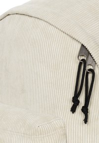 Pytel na sezení ve smetanové kordové látce s vertikálním žebrováním. Má měkkou texturu a černé stahovací šňůrky pro bezpečné uzavření.