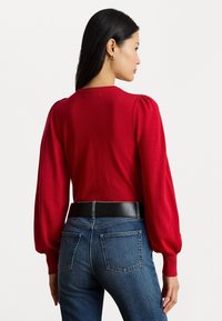 Czerwony sweter z dzianiny z bufkami, okrągłym dekoltem i ściągaczami, zestawiony z niebieskimi dżinsami o wysokim stanie oraz czarnym paskiem.