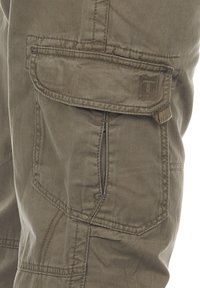 Cargo-Hosen aus olivgrünem Baumwollstoff, ausgestattet mit mehreren Taschen, verstärkten Nähten und einer strukturierten Oberfläche. Markenpatch auf der Tasche sichtbar.