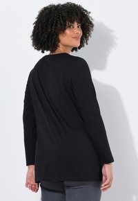 Czarna bluzka z długim rękawem, okrągłym dekoltem i bocznymi rozcięciami. Miękki, elastyczny materiał o gładkiej fakturze i luźnym kroju.