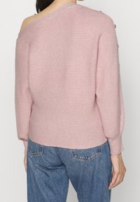 Maglione lavorato a maglia rosa chiaro con design off-shoulder e maniche ampie. Presenta dettagli con bottoni sulla spalla e una vestibilità morbida.